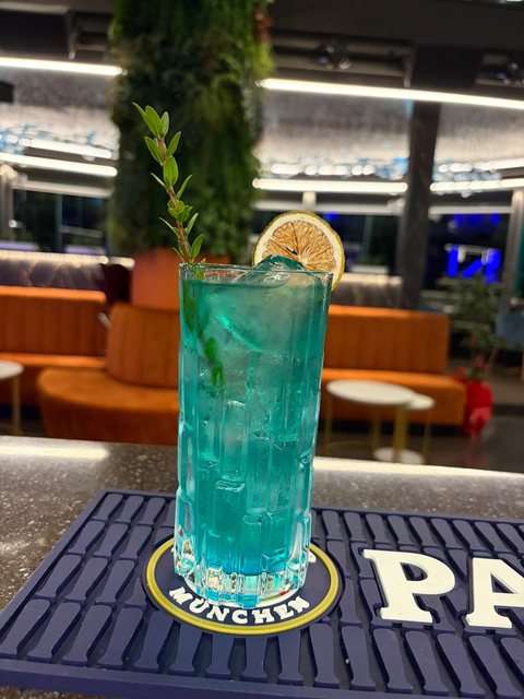 Un cocktail azzurro con ghiaccio, fetta di limone essiccato e un rametto di menta, servito al bancone di Yotto