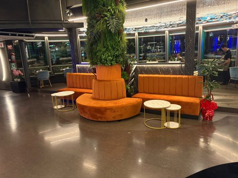 L'area lounge di Yotto con divani curvi in velluto arancione attorno alla colonna di piante e tavolini tondi in marmo e ottone