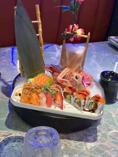 Barca di sushi con vela di foglia e bambù: sashimi di salmone e tonno, gamberi e maki, con una tazza fumante di ghiaccio secco