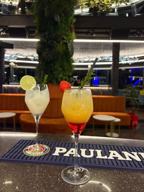Due cocktail in calice, uno chiaro con lime e uno arancione con fragola, al bancone del cocktail bar
