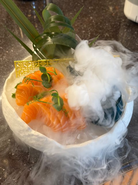 Sashimi di salmone in una ciotola bianca avvolta da una densa nuvola di ghiaccio secco, con germogli di pisello